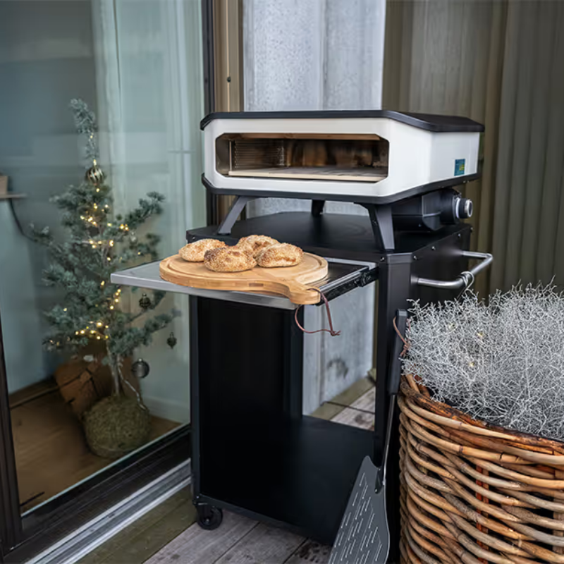 Portable pizza oven with bread on a wooden board in an indoor setting with a Christmas tree.