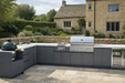 Outdoor kitchen with gray cabinets, grill, and Big Green Egg in a garden setting.